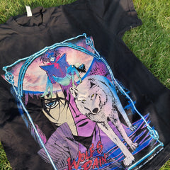 A black graphic t-shirt laid flat on green grass, featuring a large anime-style print with a wolf, a woman's face, and the text 'Wolf Rain' in red.